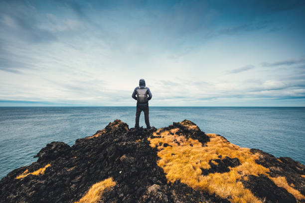 Exploring Iceland Man standing at the edge of the cliff in Iceland (starring in direction of Greenland). wonderlust stock pictures, royalty-free photos & images