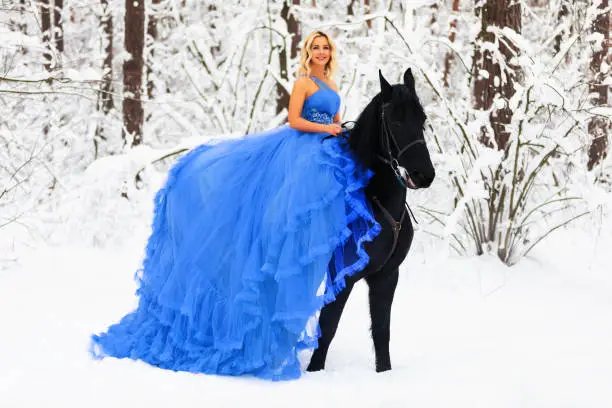 Photo of Young woman in long dress riding a horse in winter