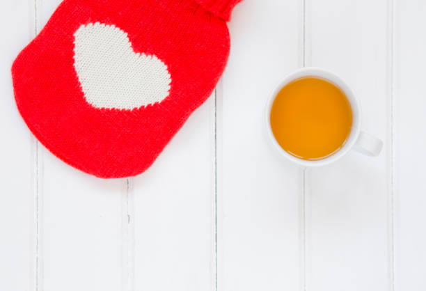 Hot water bottle and tea on wooden background