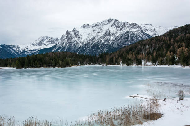 il lago ghiacciato lautersee vicino a mittenwald con montagne innevate e cielo nuvoloso - lautersee lake foto e immagini stock