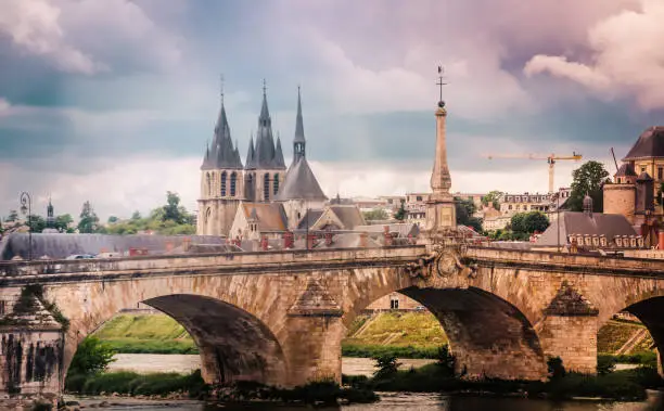 A stone bridge crosses the Loire River in Blois, France with the Blois Cathedral in the background.