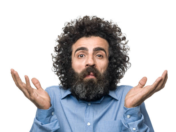 Mugshot Of Shrugging mature Adult Man Making A Face Mug shot of shrugging mature adult man making a face for curiosity. He has brown hair and beard and beard, wearing a striped blue shirt. The background is white. Shot in studio with a medium format camera. confusion raised eyebrows human face men stock pictures, royalty-free photos & images