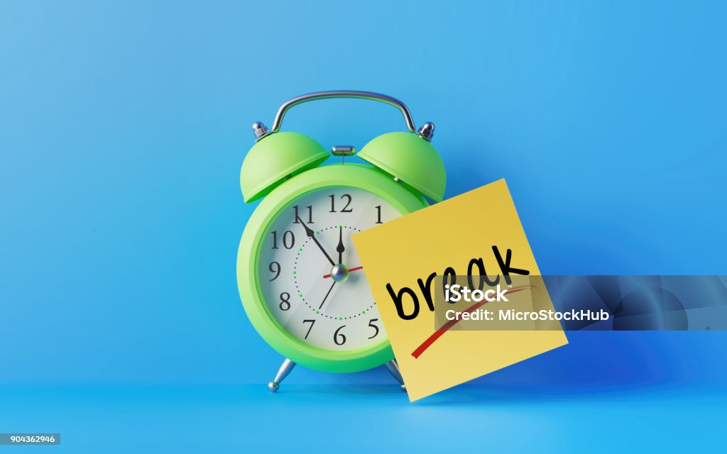 Alarm Clock And A Yellow Post It Not Over Blue Background Green alarm clock with a yellow post it note attached over bright blue background. Break writes on post it note. Reminder concept. Horizontal composition with copy space. Taking A Break Stock Photo