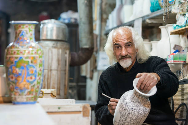 Ceramic artist is working on a piece of pottery, Iran Natanz, Iran - November 13, 2015: an elder ceramic artist and small business man is working on a piece of pottery in his small workshop. Location is the small town of Natanz, Iran. persian pottery stock pictures, royalty-free photos & images