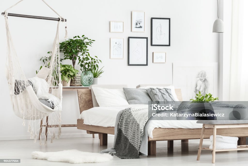 Hammock and posters in bedroom Patterned bedding on king-size bed and hammock above white fur in simple bedroom with posters Bedroom Stock Photo