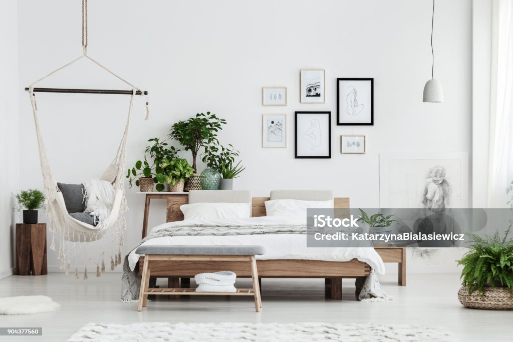 Natural bedroom with posters Hammock with blankets near plant on wooden stool and bed with white bedding in natural bedroom with posters Apartment Stock Photo