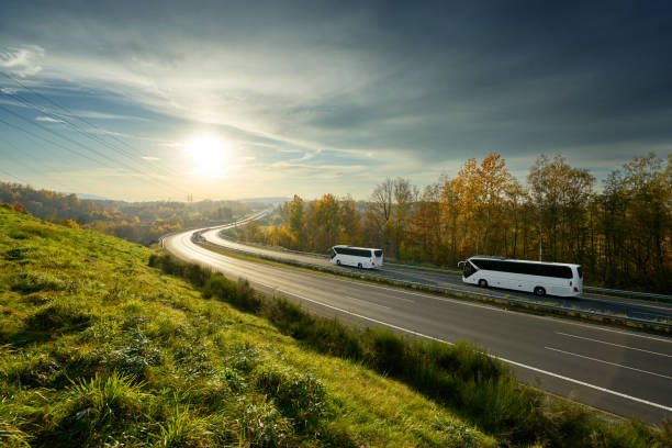 White buses traveling on the highway turning towards the horizon in an autumn landscape at sunset White buses traveling on the highway turning towards the horizon in an autumn landscape at sunset intercity train photos stock pictures, royalty-free photos & images