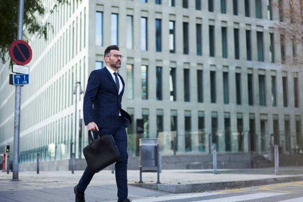 istock Confident elegantly dressed professional executive manager of company hurrying for work in morning holding suitcase crossing road in business district of city, matured lawyer strolling outdoors 904389880