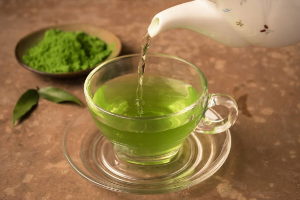 grüner tee wird in glas teetasse auf den tisch gegossen - matcha tee stock-fotos und bilder