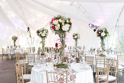 Interior of a wedding tent decoration ready for guests. Served round banquet table outdoor in marquee decorated flowers and silk. Catering concept.