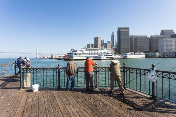 persone che pescano su un molo all'embarcadero nel centro di san francisco - san francisco county embarcadero center bay bridge built structure foto e immagini stock