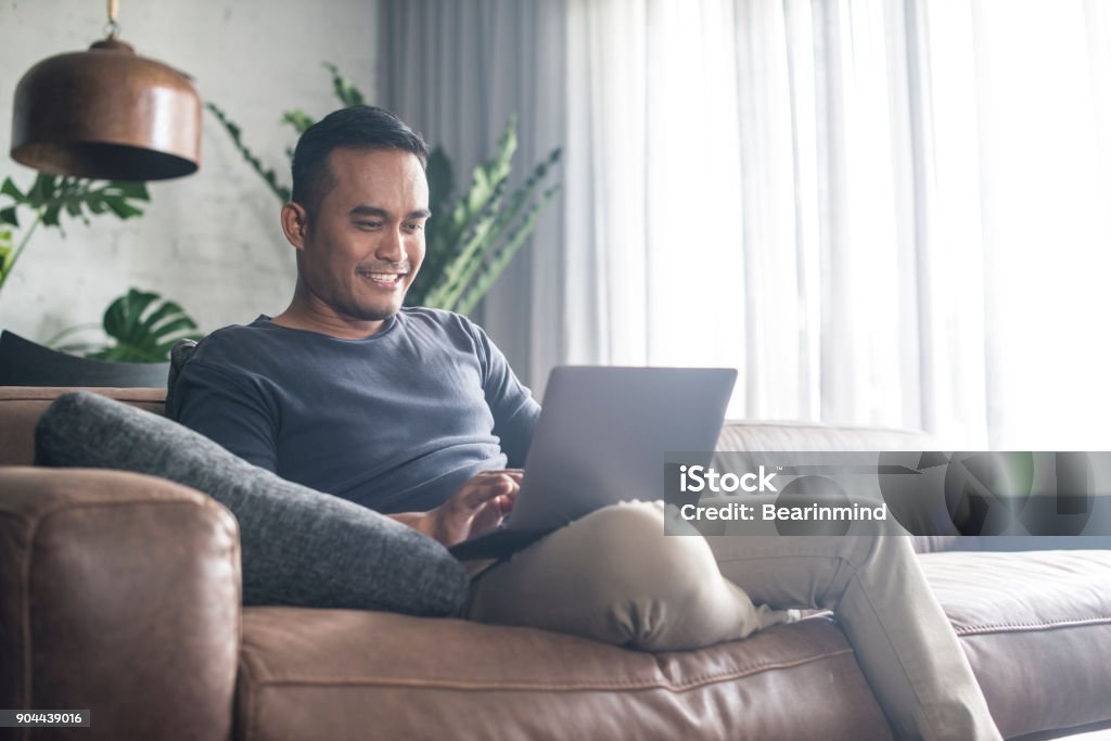 Young Asian man working at home. Young Asian man using the laptop in the living room. Laptop Stock Photo