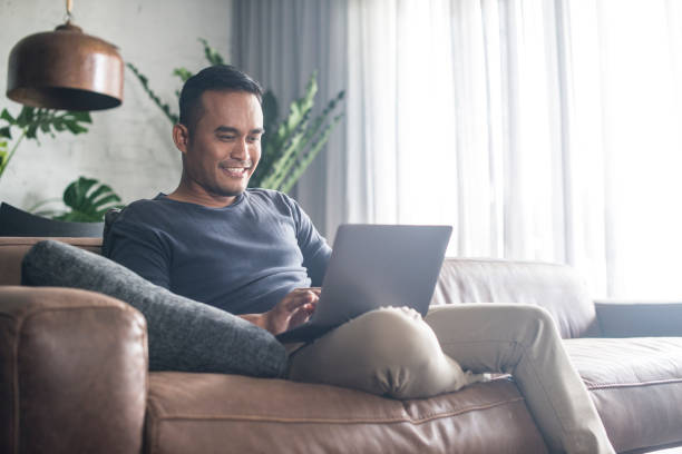 Young Asian man working at home. Young Asian man using the laptop in the living room. serene people stock pictures, royalty-free photos & images