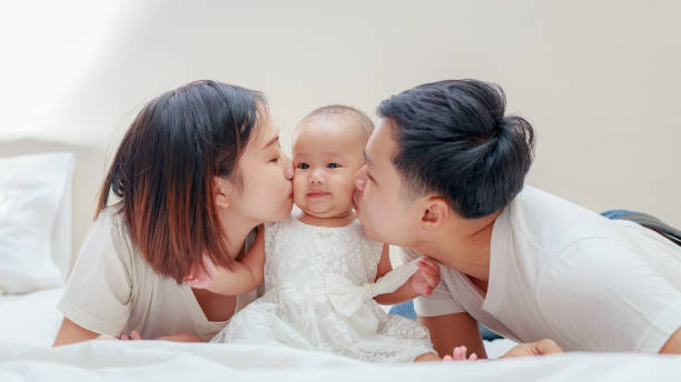 famiglia felice, giovane padre asiatico e madre che baciano la loro bambina in camera da letto - baby two parent family newborn family foto e immagini stock