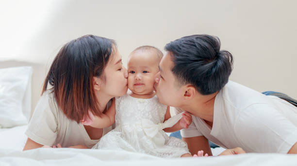 happy family, young asian father and mother kissing their baby girl on the bedroom - mother baby new kissing imagens e fotografias de stock