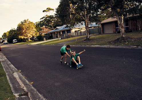 Shot of a young boy being pushed on his skateboard by his brother