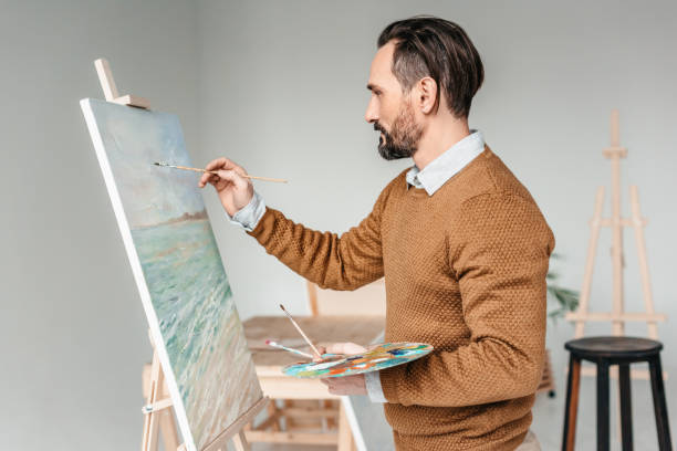 istock side view of bearded man painting on easel at art class 904457028