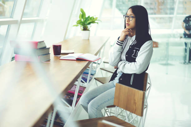 istock Thoughtful young beautiful asian student dressed in glasses learning in campus and thoughtfully thinking about new ideas. Japanese teenager female studying and preparing for exam in library interior 904460726