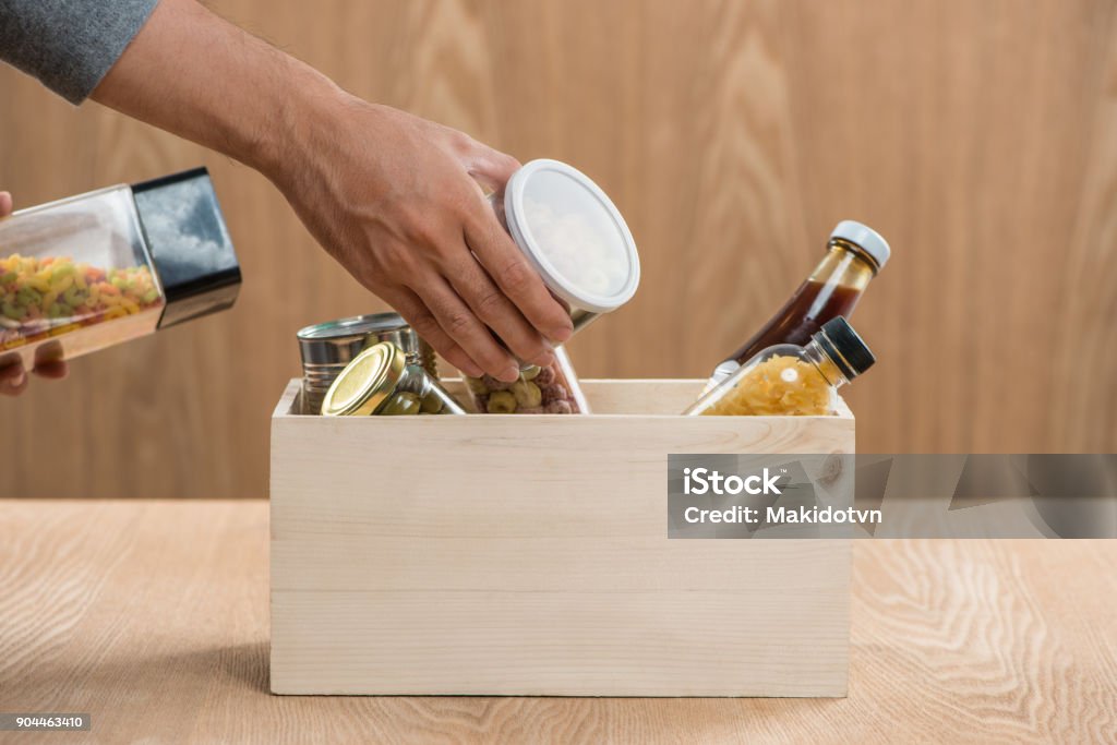 Volunteer with donation box with food stuffs on wooden background Food Stock Photo