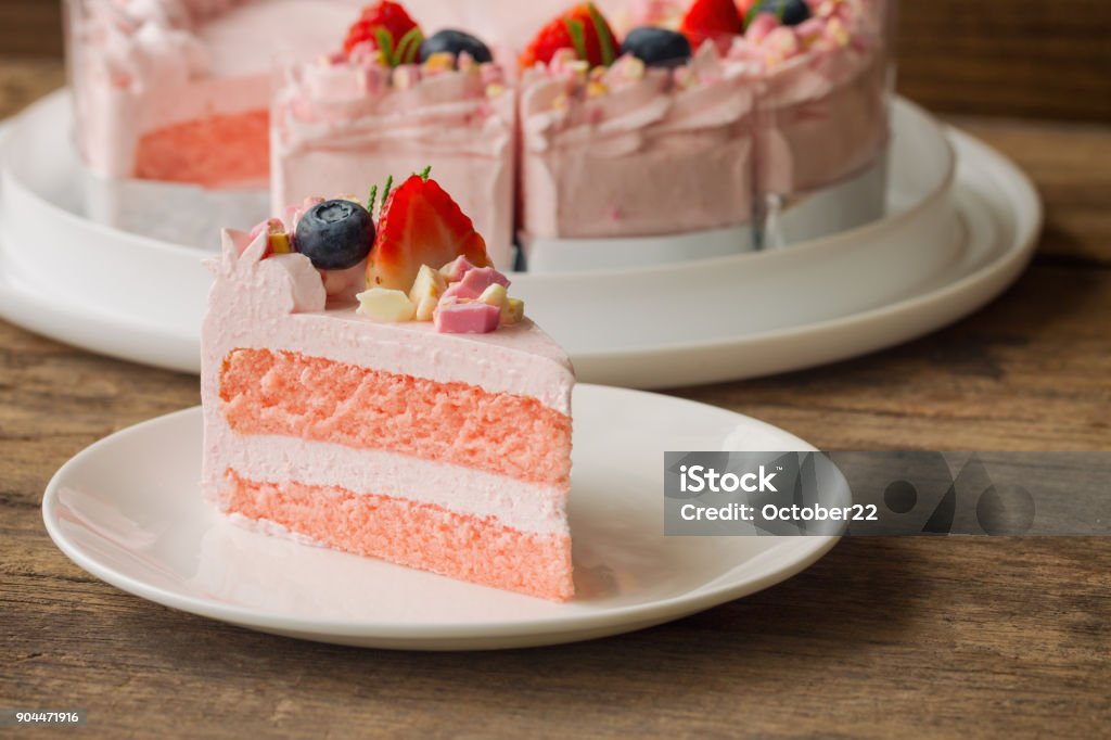 White chocolate strawberry yogurt cake decorated with fresh fruits and chocolate chunk on wood table. Delicious and sweet pink cake for Valentines or birthday party. Homemade bakery concept. Cake Stock Photo