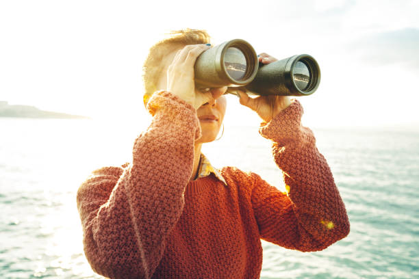 Beautiful Young Girl Looking Through Binoculars At The Sea On A Bright Sunny Day. Wanderlust Journey Concept stock photo