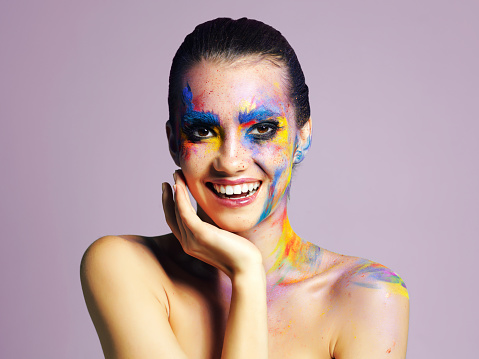 Studio shot of an attractive young woman with brightly colored makeup against a purple background