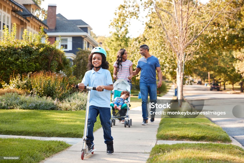 Couple Push Daughter In Stroller As Son Rides Scooter Family Stock Photo