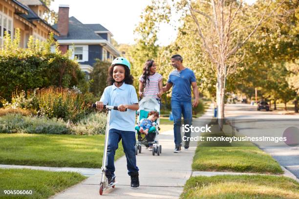 Couple Push Daughter In Stroller As Son Rides Scooter Stock Photo - Download Image Now