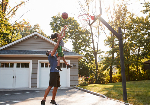 Padre e hijo jugando baloncesto en entrada de auto en casa photo