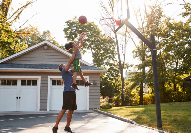 père et fils jouant au basketball sur voie d’accès à la maison - driveway photos et images de collection