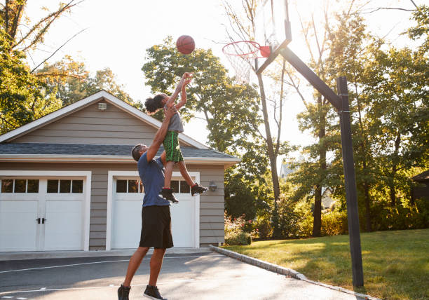 padre e figlio giocano a basket sul vialetto di casa - termine sportivo foto e immagini stock