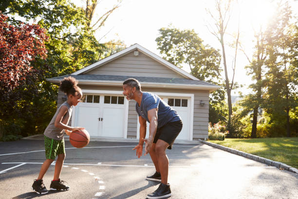 vater und sohn spielen basketball auf einfahrt zu hause - drive sportbegriff stock-fotos und bilder