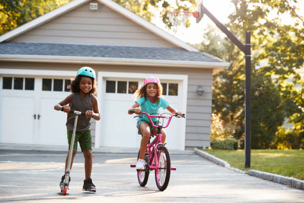 Sister With Brother Riding Scooter And Bike On Driveway At Home Sister With Brother Riding Scooter And Bike On Driveway At Home push scooter stock pictures, royalty-free photos & images