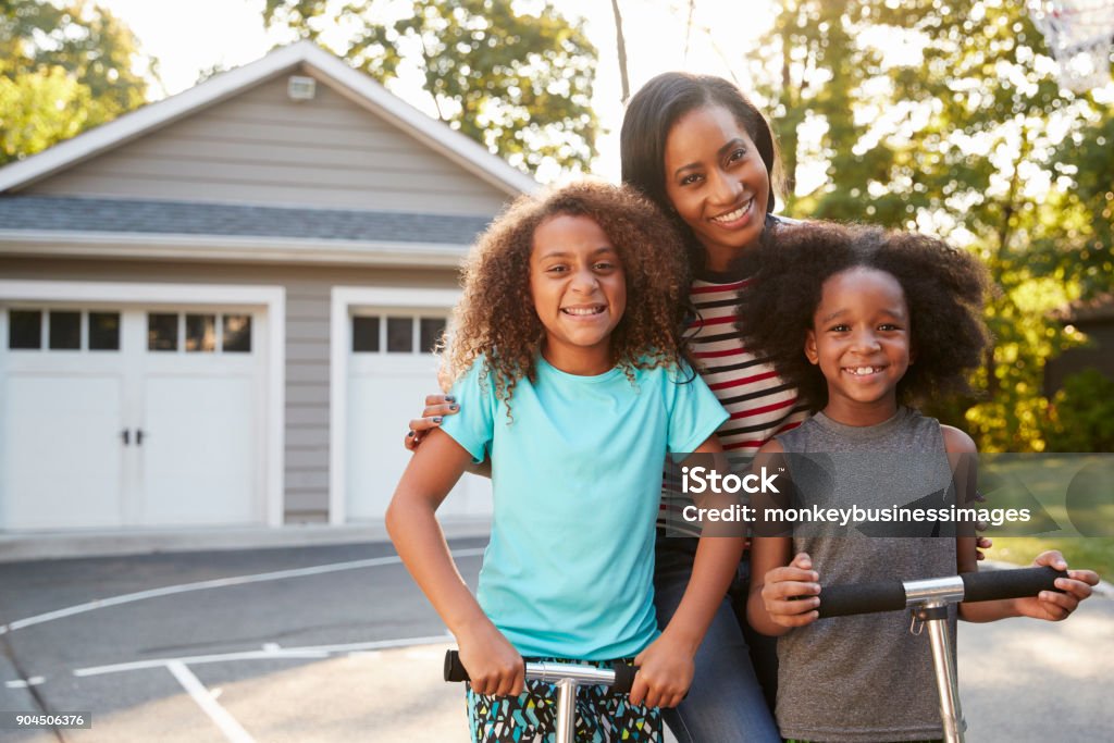 Mother With Children Riding Scooters On Driveway At Home Family Stock Photo