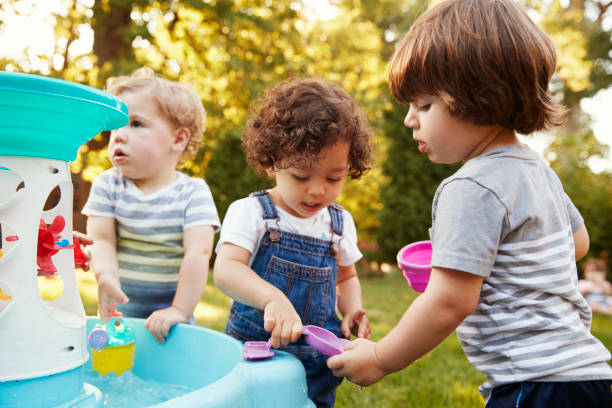 grupo de niños jugando con agua de mesa en jardín - niño pequeño fotografías e imágenes de stock