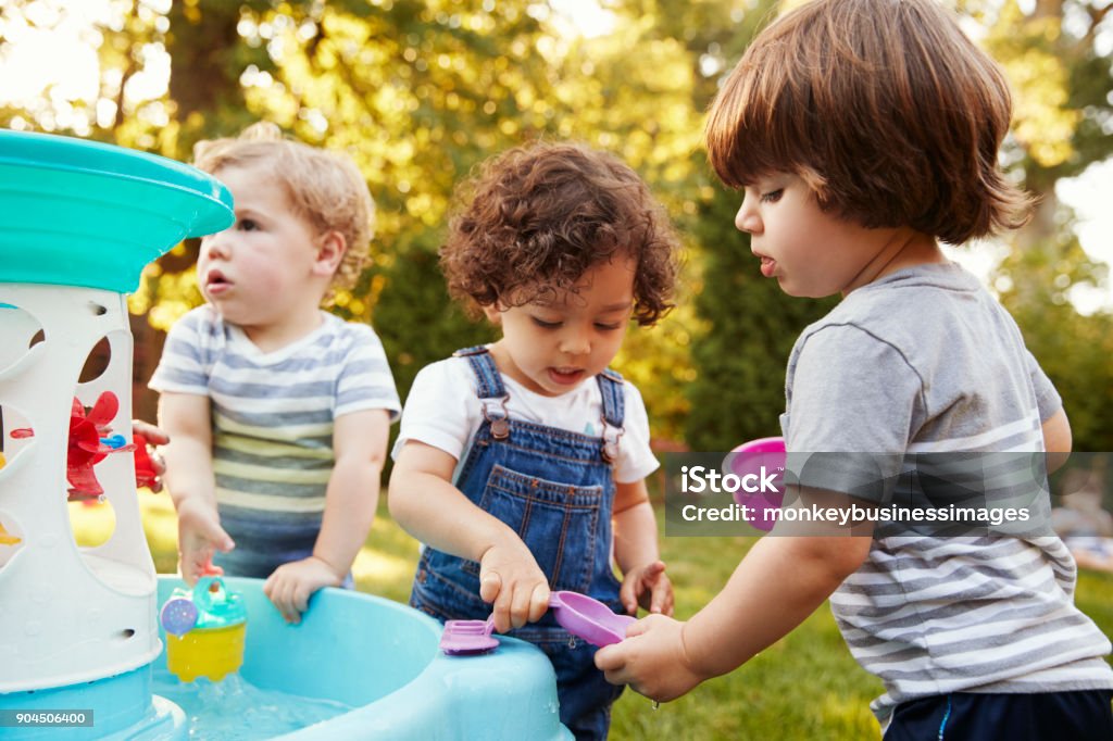 Group Of Young Children Playing With Water Table In Garden Playing Stock Photo