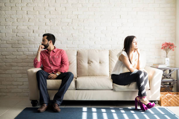 Annoyed couple ignoring each other Husband and wife sitting on the couch and not talking after an argument at home distant stock pictures, royalty-free photos & images