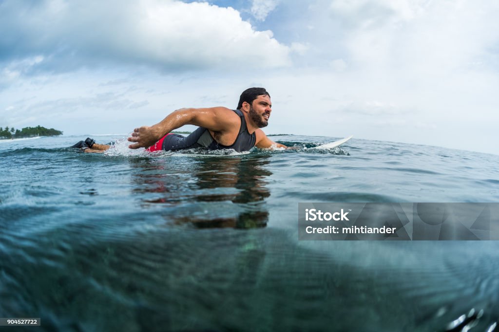 Muscular surfer paddling in the ocean Muscular surfer with beard paddling in the ocean Active Lifestyle Stock Photo