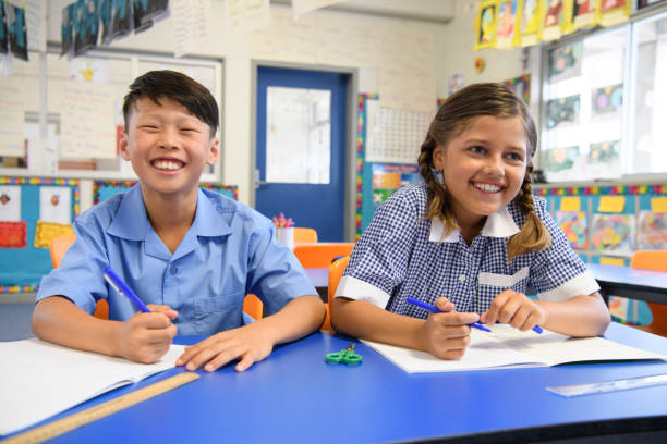 istock Two school children sitting next to each other in classroom and smiling 904531336