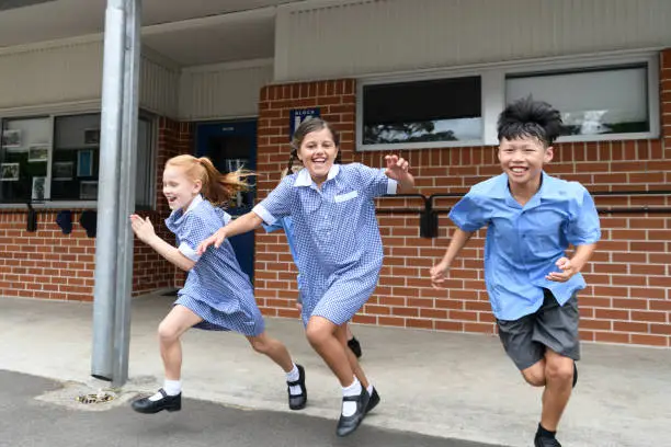 Photo of Three children running out from school across playground laughing