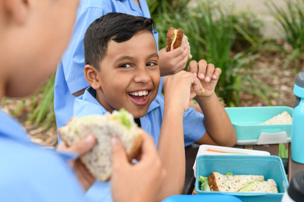 etnia boy comer almuerzo fuera con amigos de la escuela - lunch lunch box child school fotografías e imágenes de stock