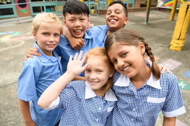 Two girls and three boys wearing school uniform smiling towards camera