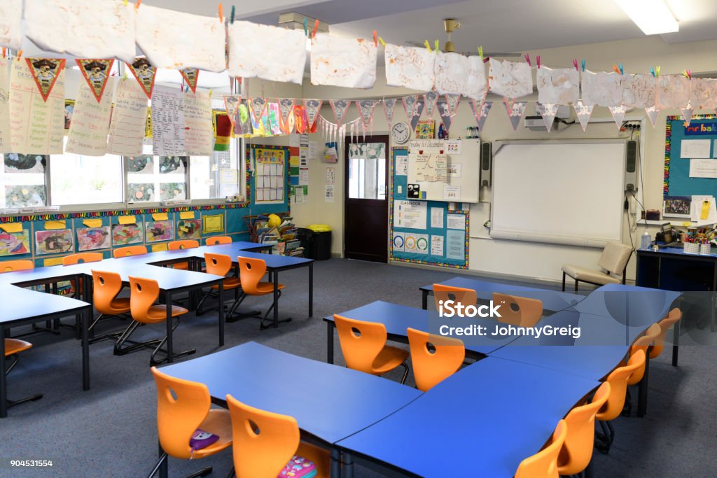Primary school classroom interior Empty tables and chairs in class with whiteboard and educational equipment. Artwork hanging up on clothes line inside Classroom Stock Photo