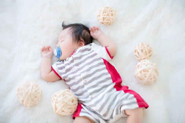 istock Cute baby is sucking pacifier and sleeping on a soft white carpet. 904539318