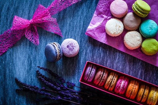 Multi colored macaroons arranged in a box shot from above on blue table. Some macaroons are out of the box placed directly on the table on pink paper napkin. Low key DSRL studio photo taken with Canon EOS 5D Mk II and Canon EF 100mm f/2.8L Macro IS USM