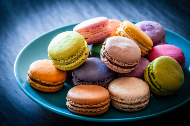 มาการองหลากสีในจานสีฟ้าที่ถ่ายบนโต๊ะสีฟ้า - macaroon ภาพสต็อก ภาพถ่ายและรูปภาพปลอดค่าลิขสิทธิ์