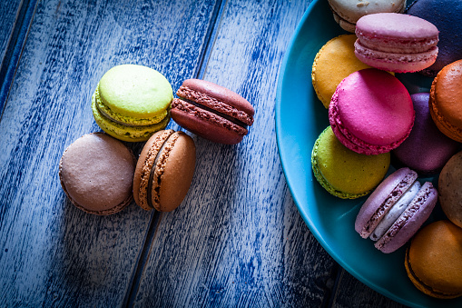 Multi colored macaroons in a blue plate shot from above on blue table. The plate is at the right and four macaroons are at the left out of the plate placed directly on the table. Low key DSRL studio photo taken with Canon EOS 5D Mk II and Canon EF 100mm f/2.8L Macro IS USM
