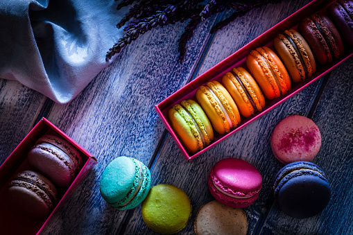 Multi colored macaroons arranged in two boxes shot from above on blue table. Some macaroons are out of one box placed directly on the table. Low key DSRL studio photo taken with Canon EOS 5D Mk II and Canon EF 100mm f/2.8L Macro IS USM