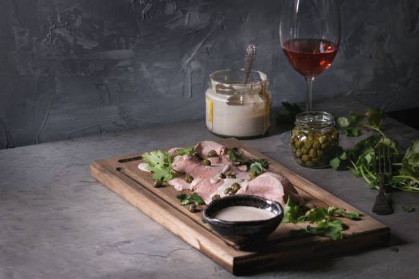 Veal with tuna sauce vitello tonnato Vitello tonnato italian dish. Thin sliced veal with tuna sauce, capers and coriander served on wooden serving board, glass of rose wine and ingredients above over gray texture kitchen table. tonatiuh stock pictures, royalty-free photos & images