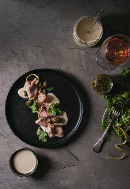 Veal with tuna sauce vitello tonnato Vitello tonnato italian dish. Thin sliced veal with tuna sauce, capers and coriander served on black plate, glass of rose wine and ingredients above over gray texture kitchen table. Top view, space tonatiuh stock pictures, royalty-free photos & images
